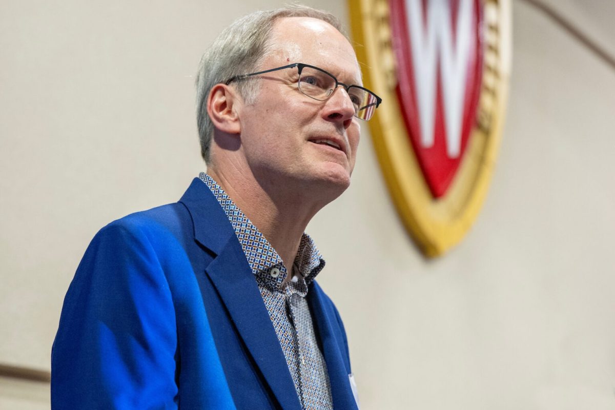 A closeup of a white man with short gray hair and glasses speaking to an audience