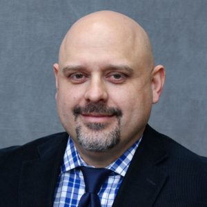 headshot of a bald man with light skin and a gray goatee